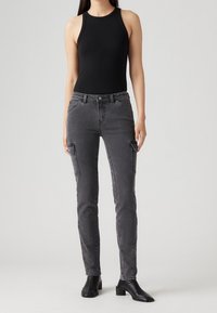 Bodysuit negro con textura acanalada combinado con jeans cargo grises que cuentan con bolsillos laterales, diseño ajustado y un leve desvanecimiento. Completado con botas negras hasta el tobillo.
