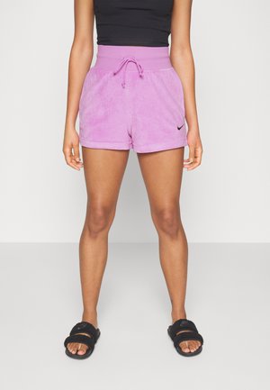 Pantalones cortos de forro polar rosa con una cintura alta y cordón, con un pequeño logo de Nike en negro en el lateral. Sandalias de playa negras puestas.