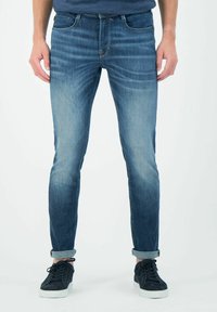 Vaqueros de denim azul con un ajuste slim, diseño ligeramente desgastado y puños enrollados. Combinados con zapatillas oscuras para un look informal.
