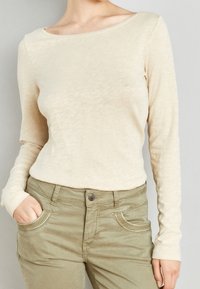 Beige top met lange mouwen van een zachte, gestructureerde stof met een brede halslijn, gecombineerd met olijfgroene broek met gestikte zakaccenten.