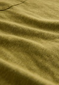 Textiel in olijfgroen met een zachte, gestructureerde oppervlakte, die zachte plooien en kreukels toont, wat duidt op flexibiliteit en de dikte van de stof.