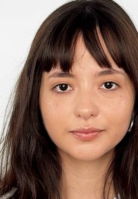 Retrato de una persona con cabello largo castaño oscuro y flequillo, que lleva un ligero brillo en los labios y grandes pendientes circulares.