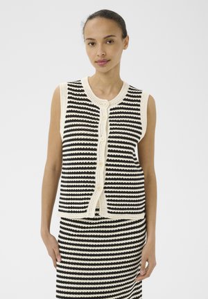 Kvinde iført en ærmeløs sort-hvid stribet strikvest med knapper over et matchende stribet striknederdel.