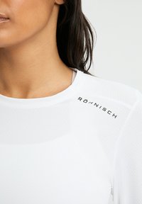 Weißes Sportoberteil aus strukturiertem Stoff, mit rundem Halsausschnitt, Röhnisch-Logo auf der Schulter und glattem, tailliertem Design.