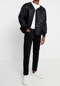 Musta tikattu bomber-takki pyöreällä kauluksella, nappisuljinnalla ja resoreilla hihojen suissa, valkoisen t-paidan päällä, yhdistetty mustiin farkkuihin ja valkoisiin tennareihin.