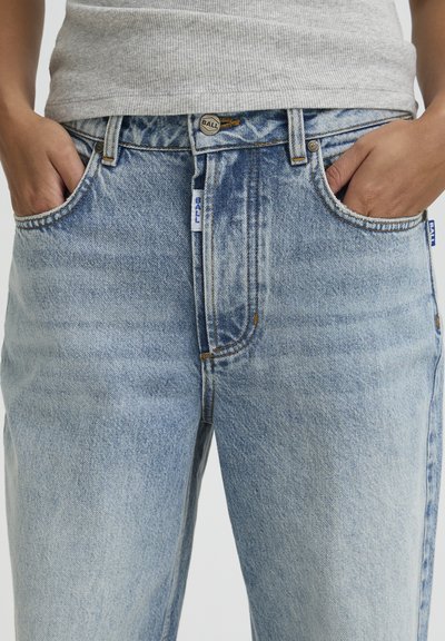 Svetlomodré džínsové nohavice s klasickým strihom. Majú päť vreciek, kontrastné šitie a zapínanie na kovový gombík.