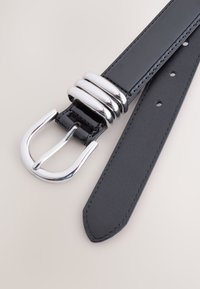 Ceinture en cuir noir avec une boucle argentée brillante ornée de trois accents ronds, texture lisse et design à pointe.