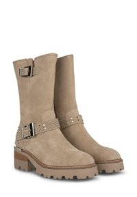 Bottines en cuir suède beige avec une semelle épaisse, des boucles décoratives sur les côtés et des détails de sangles studées. Talon plat et finition texturée.