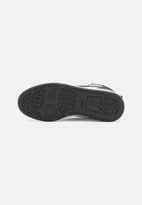 Zwarte sport schoen zool met een getextureerd rubber patroon. Beschikt over een cirkelvormig gripontwerp en het merkembleem op de hak.