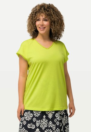 Limegrøn V-hals T-shirt med korte ærmer, der har dekorativ syning langs halsudskæringen og ærmekanterne. Sammen med et mønstret nederdel.