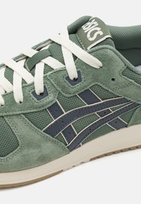 Baskets en suède vert et en mesh avec des lacets blancs, des accents vert foncé et une semelle beige. Présente un logo sur la languette et un design rayé.