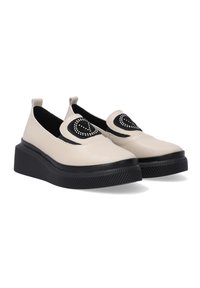 Beige Slipper mit einem schwarzen Akzent, der ein Herzdesign und Nietenverzierungen aufweist, auf einer strukturierten schwarzen Plateausohle.