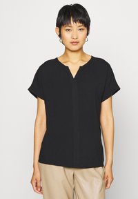Must mustärg blouse lühikeste varrukatega ja V-kaelusega, valmistatud siledast kangast, esiosas on õmbluse detail ja lõdva silueti kujundus.