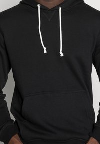 Sudadera negra con capucha y cordones blancos, bolsillo frontal tipo canguro, puños acanalados y una suave tela de mezcla de algodón.