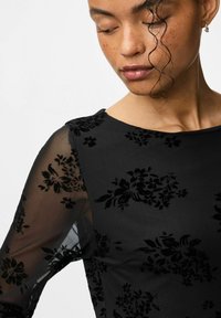 Zwart bloemenjurk met doorschijnende lange mouwen. De textuurstof heeft reliëf bloemenpatronen. Ronde halslijn, getailleerde pasvorm.