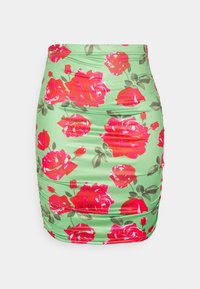 Mini saia floral com tecido verde, decorada com rosas vermelhas vibrantes e folhas verdes, laterais franzidas e um design ajustado.