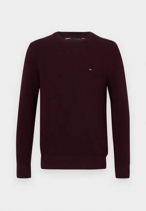 Burgundowy sweter z okrągłym dekoltem, długimi rękawami, ściągaczami na mankietach oraz małym logo na piersi. Wykonany z teksturowanej dzianiny.