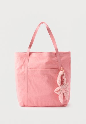 Roze canvas tas met twee handvatten en een aangehechte roze stoffen scrunchie in de vorm van een blad, op een witte achtergrond.