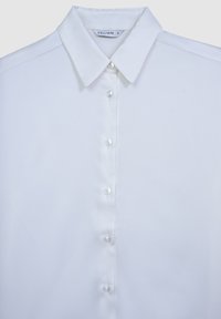Camicia bianca con bottone realizzata in tessuto lucido, caratterizzata da un colletto classico e sei bottoni perlacei lungo la parte anteriore. Design minimalista.