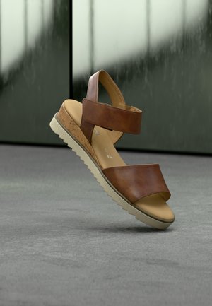 Bruine leren sandaal met twee brede banden, een kurkaccent op de zool en een beige rubberen buitenzool met een zigzagpatroon.