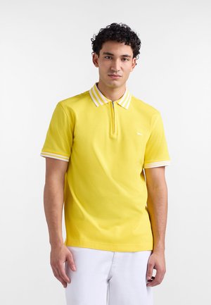 Yellow polo shirt with a zip collar, featuring white and yellow striped detailing on the collar and sleeve hems. Soft fabric texture.
