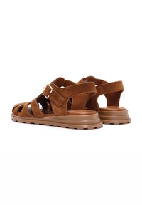 Sandalias de ante marrón con múltiples correas, una hebilla en el tobillo y una suela a contraste con un patrón de relieve texturizado.