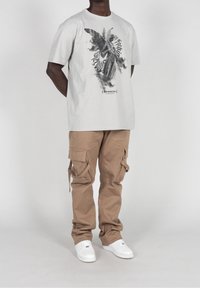 Camiseta de algodón gris claro con un diseño gráfico negro que presenta una mariposa y texto, combinada con pantalones cargo color caqui y zapatillas blancas.