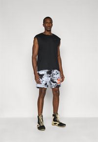 Μαύρη αμάνικη μπλούζα, γκρι και μαύρο σορτς με σχέδιο, πορτοκαλί λεπτομέρεια. Μαύρα ψηλά αθλητικά παπούτσια με ανοιχτόχρωμη σόλα. Έμφαση σε σπορ casual στυλ.