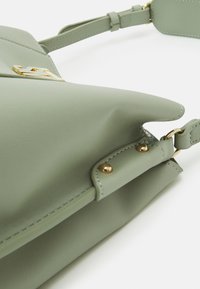 Zielona torebka z ekologicznej skóry o uporządkowanym designie, z złotymi elementami ozdobnymi i akcentami przeszycia. Posiada regulowany pasek.