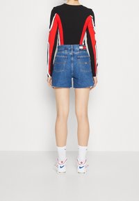 Černý top s dlouhým rukávem s červenými a bílými akcenty, doplněný vysokými džínovými šortkami. Šortky mají třepení na lemu a zadní kapsy.