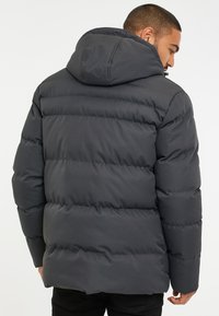 Puffjacka i mörkgrått, med huva, kviltad design och slät yta. Baksidan visar en avslappnad passform med elastiska detaljer.