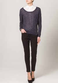 Maglione blu navy a maglia con un ampio scollo, indossato sopra una camicia bianca con colletto. Abbinato a pantaloni neri slim e tacchi alti neri.