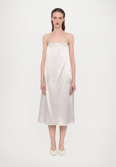 Robe en satin à bretelles fines, décolleté droit et silhouette évasée fluide en argent pâle. Les chaussures présentent des bouts pointus.