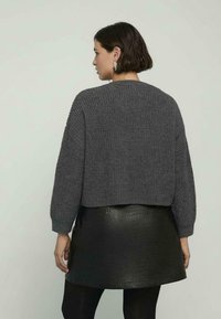 Przycięty szary sweter z dzianiny o teksturowanym wzorze, z prążkowanymi mankietami i szerokim dekoltem, w połączeniu z czarną skórzaną spódnicą mini z wzorem węża.