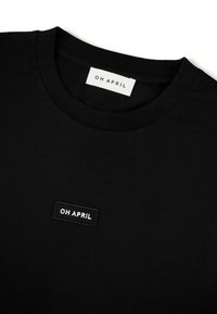 Svart bomulls t-shirt med rund hals. Har en sydd rektangulär etikett som står "OH APRIL" i vitt på framsidan. Enkel design.