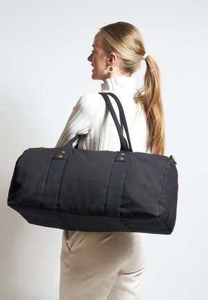 Borsa a duffel nera realizzata in tessuto resistente, con due robusti manici e dettagli in metallo. Caratterizzata da una forma cilindrica e una base piatta.