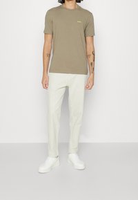 Olivgrön bomulls t-shirt med korta ärmar och liten logotyp, i kombination med ljusbeige byxor och vita sneakers. Enkel, avslappnad design.