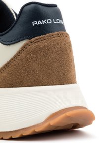 Brązowe zamszowe i białe gumowe sneakersy z czarnymi skórzanymi akcentami. Wyposażone w teksturowaną podeszwę oraz branding "PAKO LOREN" na pięcie.