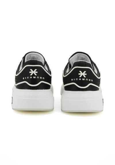 Zapatillas negras con suelas blancas, que cuentan con un cuello acolchado, una marca en el talón y una parte superior texturizada. Parte trasera reforzada para mayor soporte.