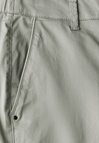 Světle šedé kalhoty vyrobené z měkkého materiálu s hladkou strukturou, diagonální kapsou se švy a kovovým zámkem.