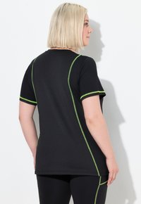 Top negro de manga corta con costuras verdes a contraste. Cuenta con cuello redondo y silueta ajustada, combinado con leggings negros.