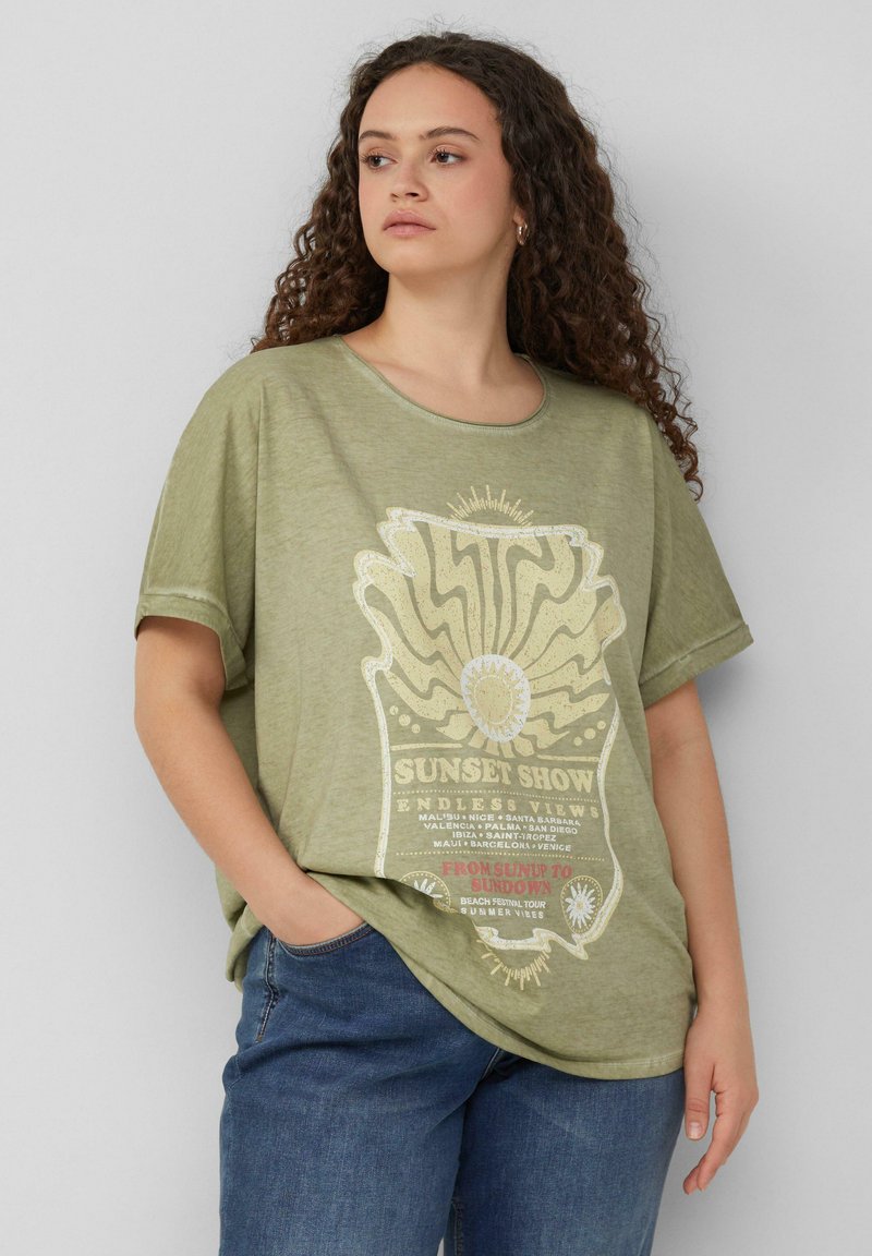 Olivegrünes, übergroßes T-Shirt, kurze Ärmel, runder Halsausschnitt. Auf der Front befindet sich ein grafisches Vintage-Motiv mit weißem und rotem Text.