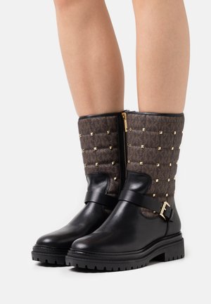 Zwarte leren enkelboots hebben een gewatteerde bovenkant van bruin stof met gouden studs en een zijknop. De rubberen zool biedt grip.