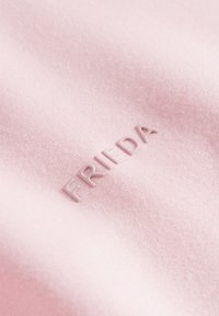 Pink fabric featuring textured "FRIEDA" branding in a slightly raised, matte finish. Soft, cotton-like texture with a smooth appearance.