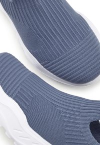Scarpe slip-on in tessuto blu lavorato a maglia con texture a coste, parte superiore elastica e suola in gomma bianca. Presentano una punta rotonda e un design minimalista.