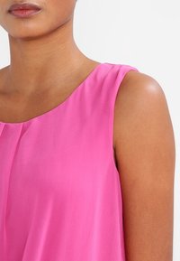 Różowa bluzka bez rękawów o miękkiej, gładkiej fakturze, z okrągłym dekoltem i delikatnymi fałdami, uchwycająca żywy kolor i elegancki design.
