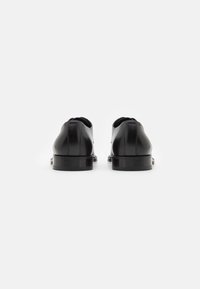Scarpe in pelle nera con finitura liscia, punta arrotondata e tacco basso, caratterizzate da un design minimalista senza hardware o accenti visibili.