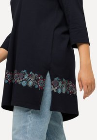 Marinefarbener Tunika mit floraler Stickerei in Rot, Blau und Grau am Saum, mit einem Schlitzdetail und drei Viertelärmeln.