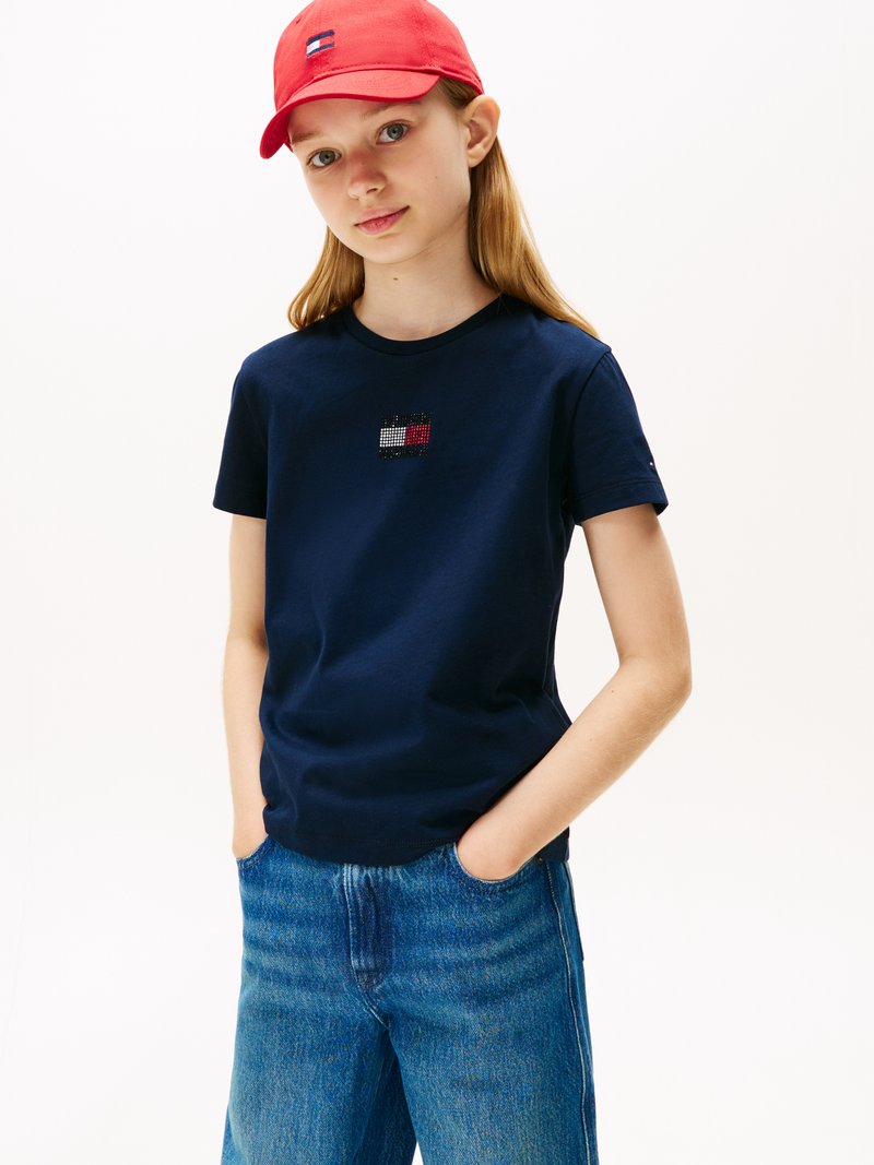 Mørkeblå bomull t-skjorte med en liten brodert flagglogo; kombinert med lyseblå vide jeans og en rød caps.