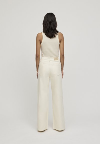 Pantaloni a gamba larga color crema con una finitura leggermente testurizzata e vita alta, abbinati a un top aderente color crema, vista posteriore.